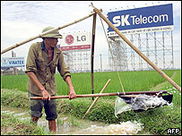 A farmer uses a traditional way to water his rice field next to huge advertising posters for local and foreign companies in the suburbs of Hanoi, 23 July 2002.  